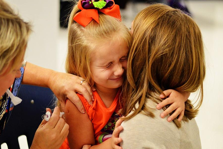 First+grader+Piper+White+receives+her+flu+shot+while+being+comforted+by+her+teacher+Stephanie+Decker.+Elementary+and+high+school+students+received+their+flu+shots+from+the+Craighead+County+Health+Department+on+Wednesday.+